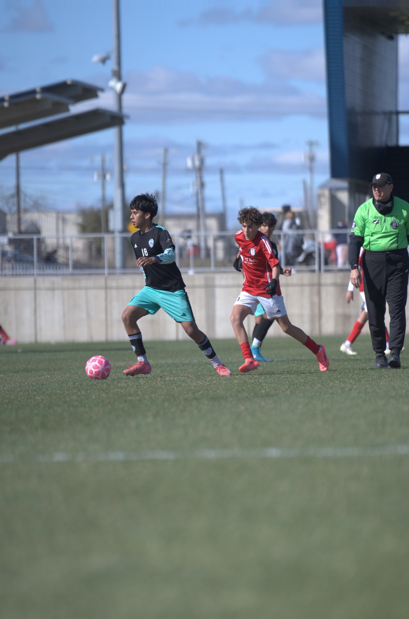 Youth players chasing a pink soccer ball during a match