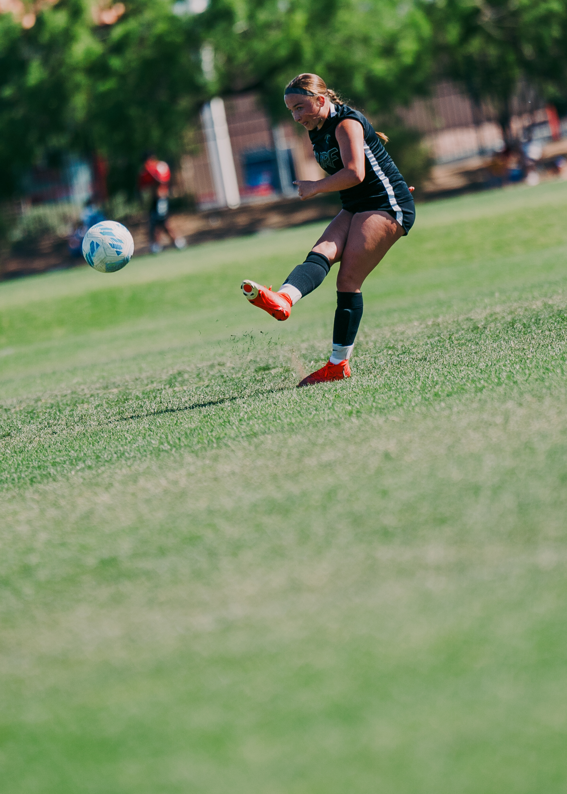 Girl in a dark uniform striking the soccer ball at a Tiger tournament