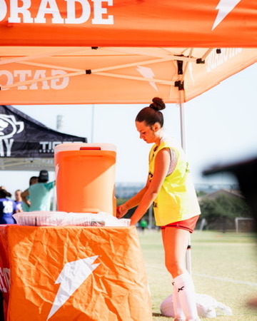 Soccer player visiting the Gatorade station under an orange tent